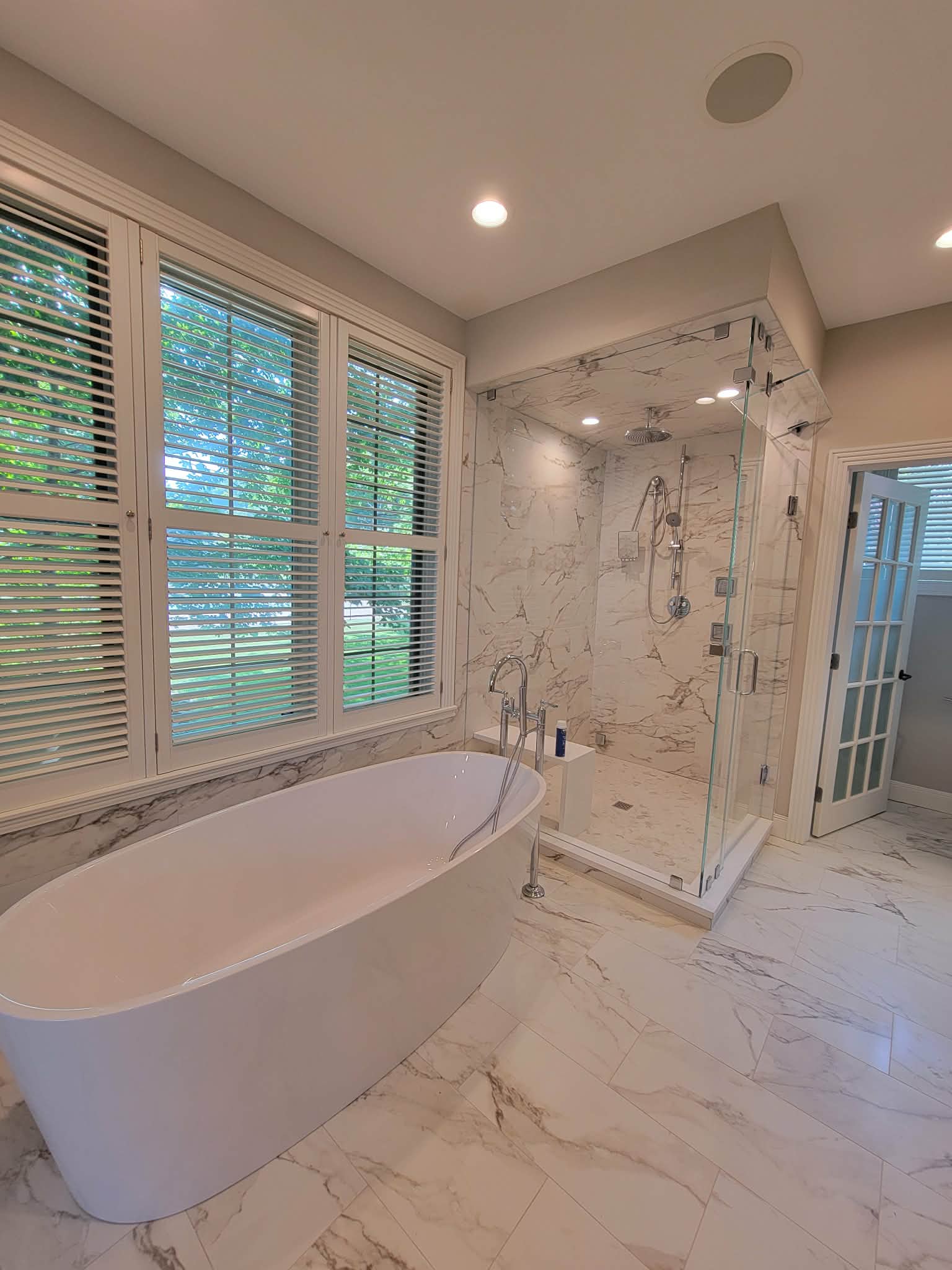 Bathroom with a freestanding tub, glass shower and marble-pattern tile