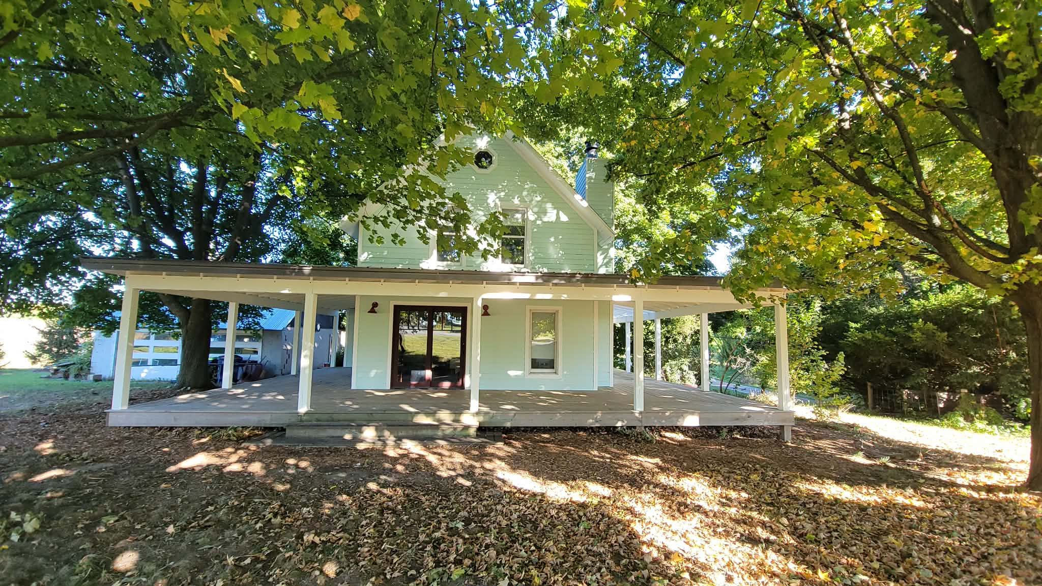 Pale green cottage with a wraparound porch beneath mature trees