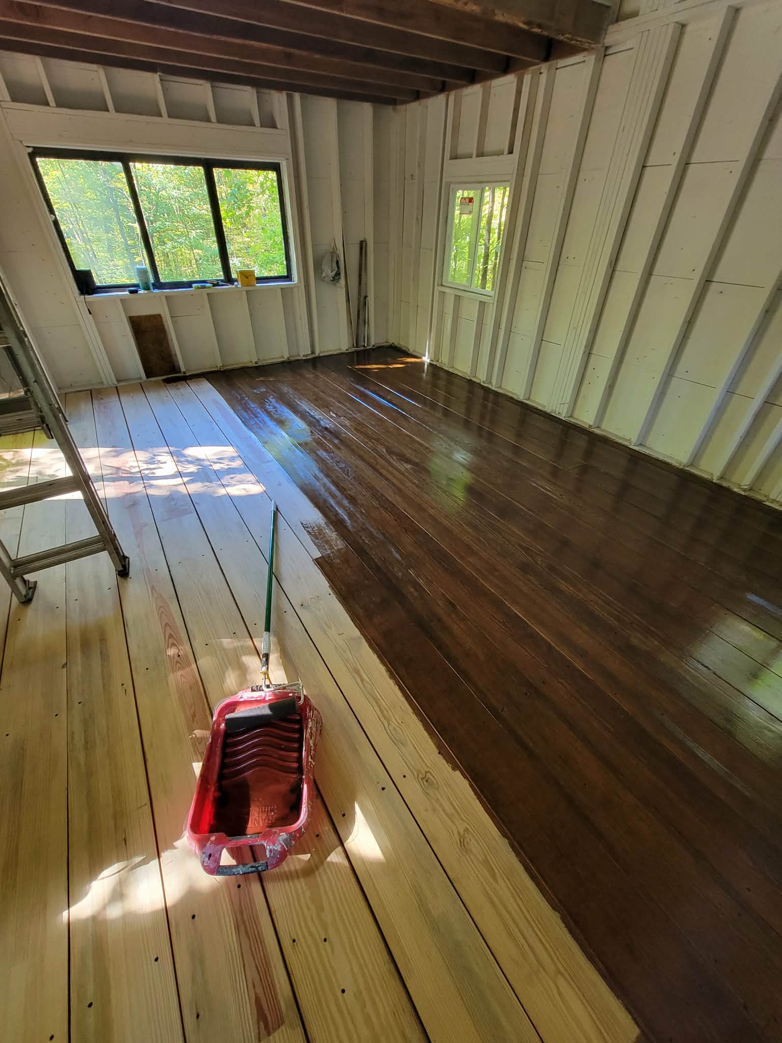 Wood floor during staining, with a roller and rich brown finish