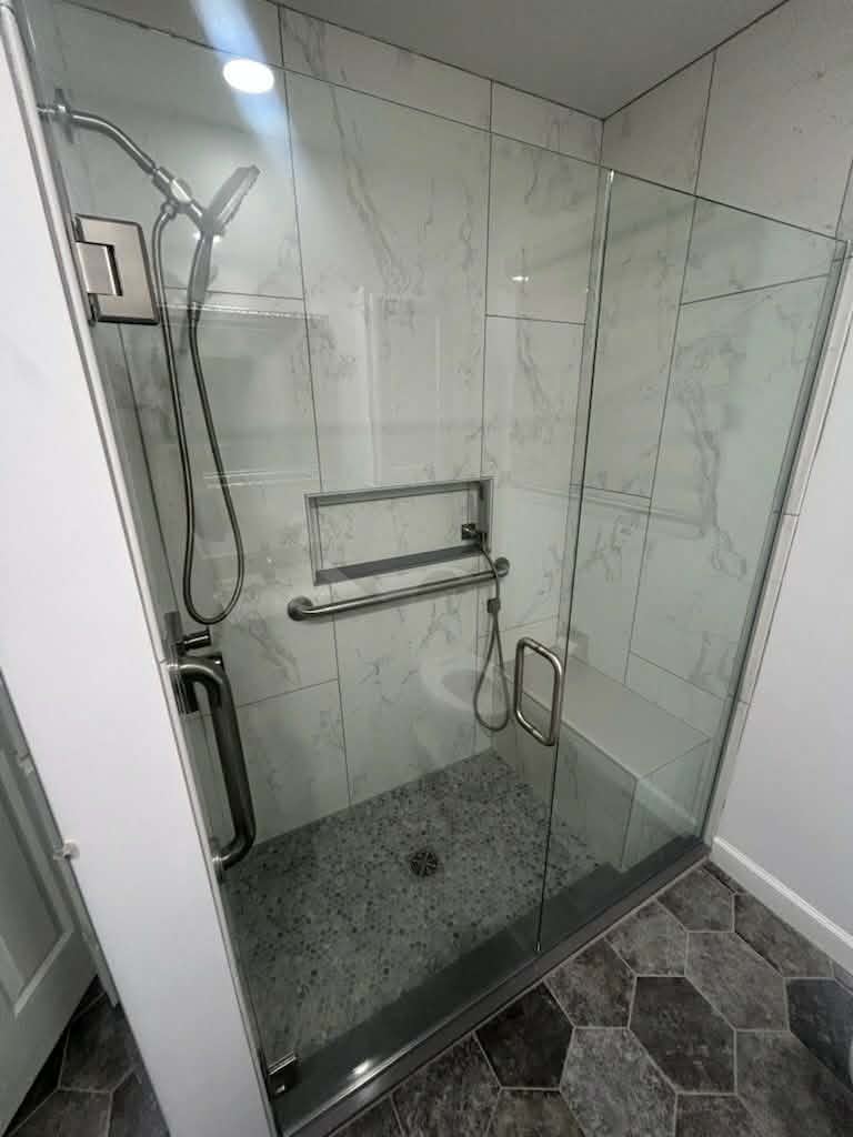 Glass shower with tile walls, a recessed shelf and grab bars