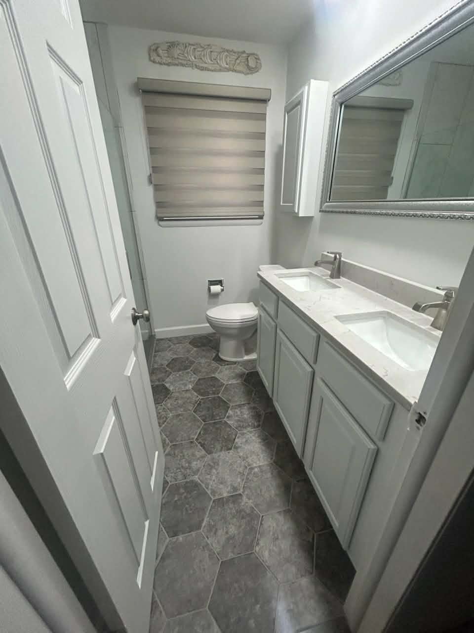 Bathroom with a double vanity, light cabinetry and patterned tile floor